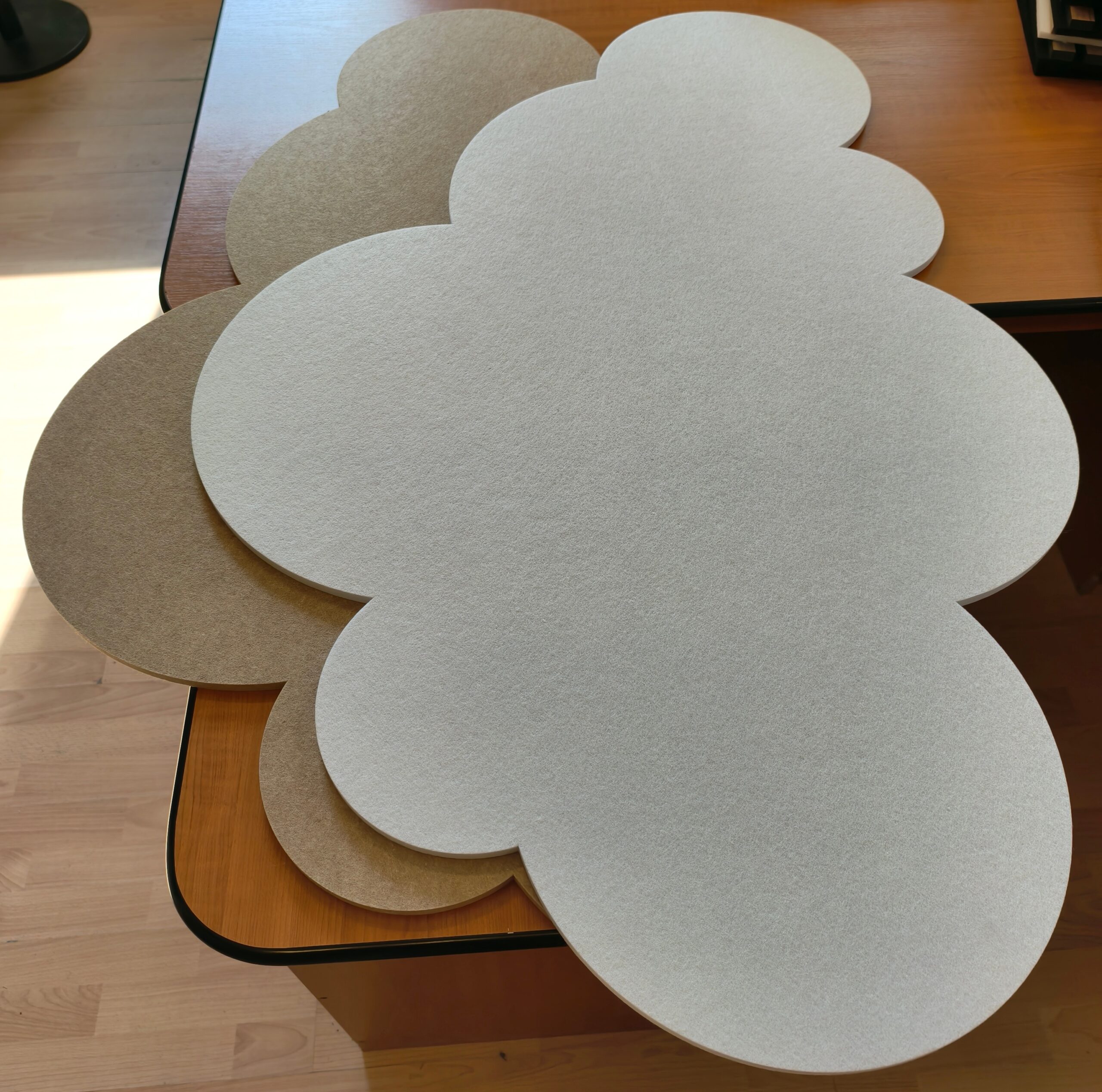 Paneles acústicos de techo Bilnora con forma de nube en colores blanco y camel sobre una mesa