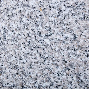 Primer plano del granito natural Bianco Sardo, con una superficie moteada en blanco y gris y pequeñas inclusiones minerales negras distribuidas de forma irregular.