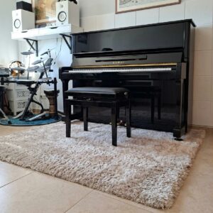 professional-calm-beige-alfombra-oficina-en-casa-musica Alfombra Professional Calm Beige colocada bajo un piano en una habitación de música y trabajo, mostrando su superficie suave y de pelo largo.